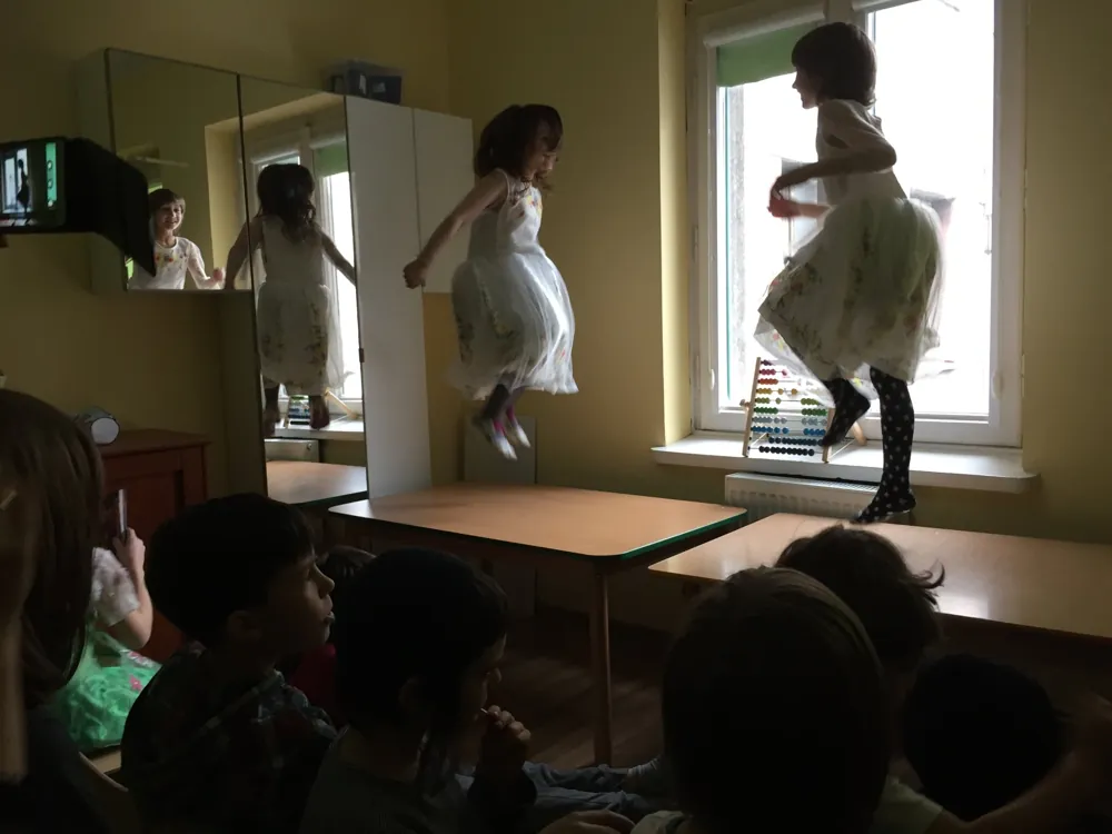 Dziewczynki tańczą i skaczą podczas występu, reszta grupy ogląda